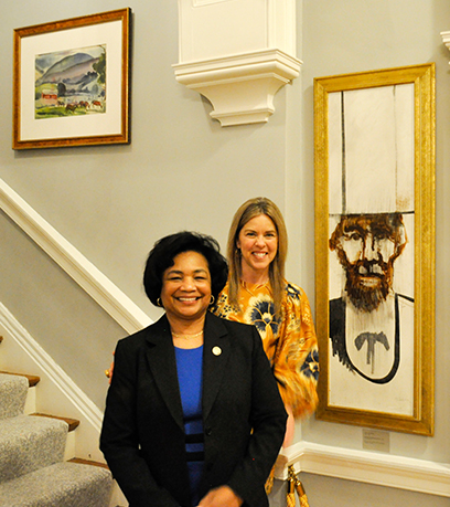 Two women standing next to a contemporary portrait of Abraham Lincoln.