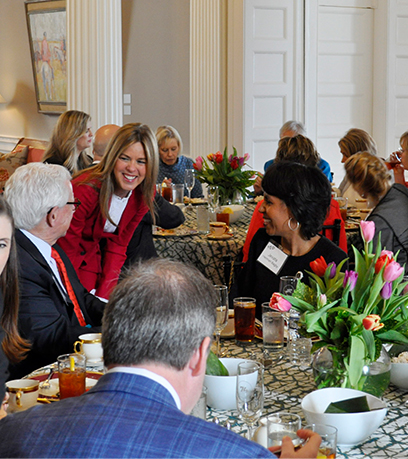 First Lady Suzanne S. Youngkin bends down to greet a man and woman sitting at a table.