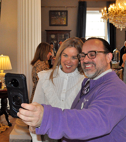 First Lady Suzanne S. Youngkin and a man in a purple sweater pose for a selfie.