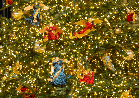 Five angle ornaments, two wearing blue and three wearing red in cluster on tree