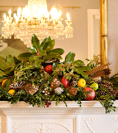 A mantle is decorated with magnolia leaves, feathers, fruit, holly berries and more.