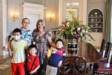 The First Lady poses with a family in front of the Dining Room table arrangement.