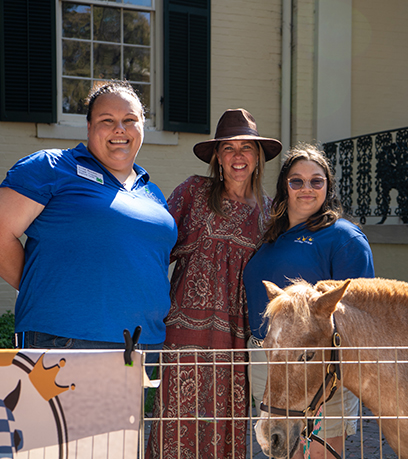 The First Lady poses with two horse trainers wearing and a miniature horse named cinnamon.