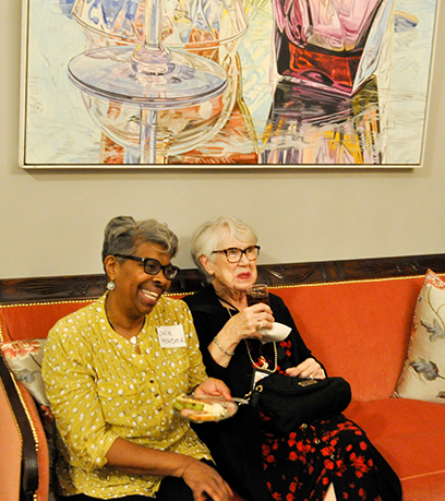 Two ladies laughing and smiling while sitting together on a red couch.