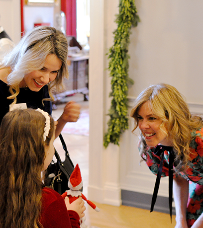 First Lady Suzanne Youngkin bends down to greet a young girl as her mother smiles.