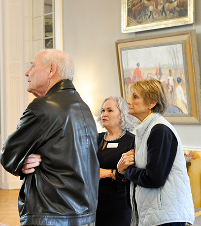 Three people standing, looking to the right with paintings in the background.