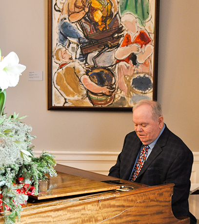 A man sits behind a piano with a painting in the background.