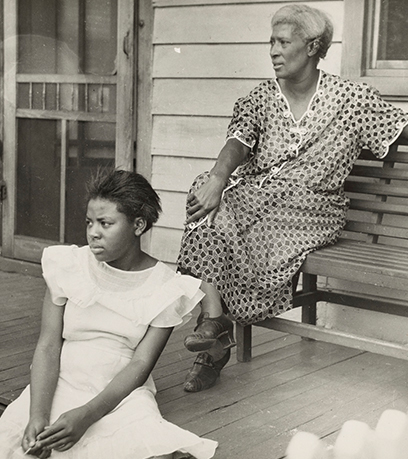 A black and white photograph taken by Robert McNeill of a young girl and her grandmother sitting on their porch.