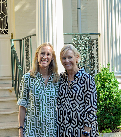 Two women stand in front of the Executive Mansion wearing geometric dresses.