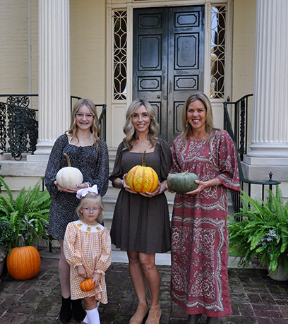 The First Lady and three women of various ages stand in front of the Executive Mansion holding pumpkins of various colors.