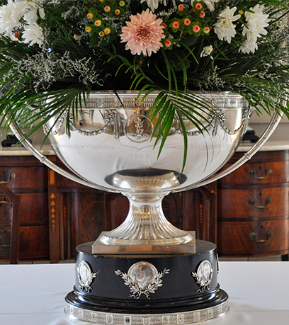 A silver punch bowl filled with a floral arrangement on a white table cloth.